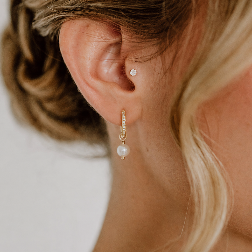 Feine Brautcreolen aus 925er Sterlingsilber 18K vergoldet, mit Zirkonia Kristallen und darunter hängender runder veganer Perle, detailreich am Ohr eines Models mit romantischer Hochsteckfrisur getragen.