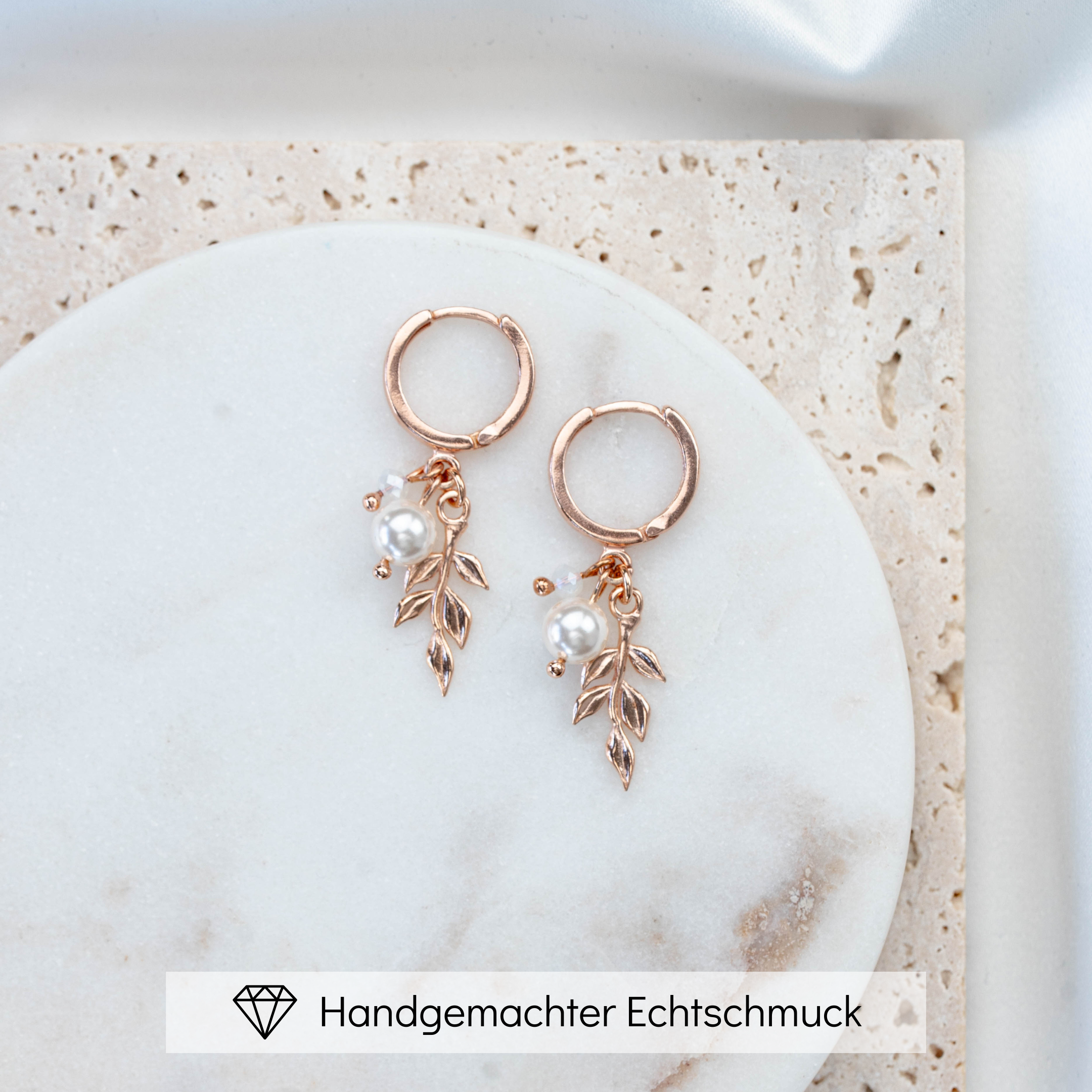 Braut Creole aus 925 Sterlingsilber, 18K rosévergoldet, mit zartem Blattanhänger, weißer Perle und white opal Kristallperle, liegend auf Marmorplatte