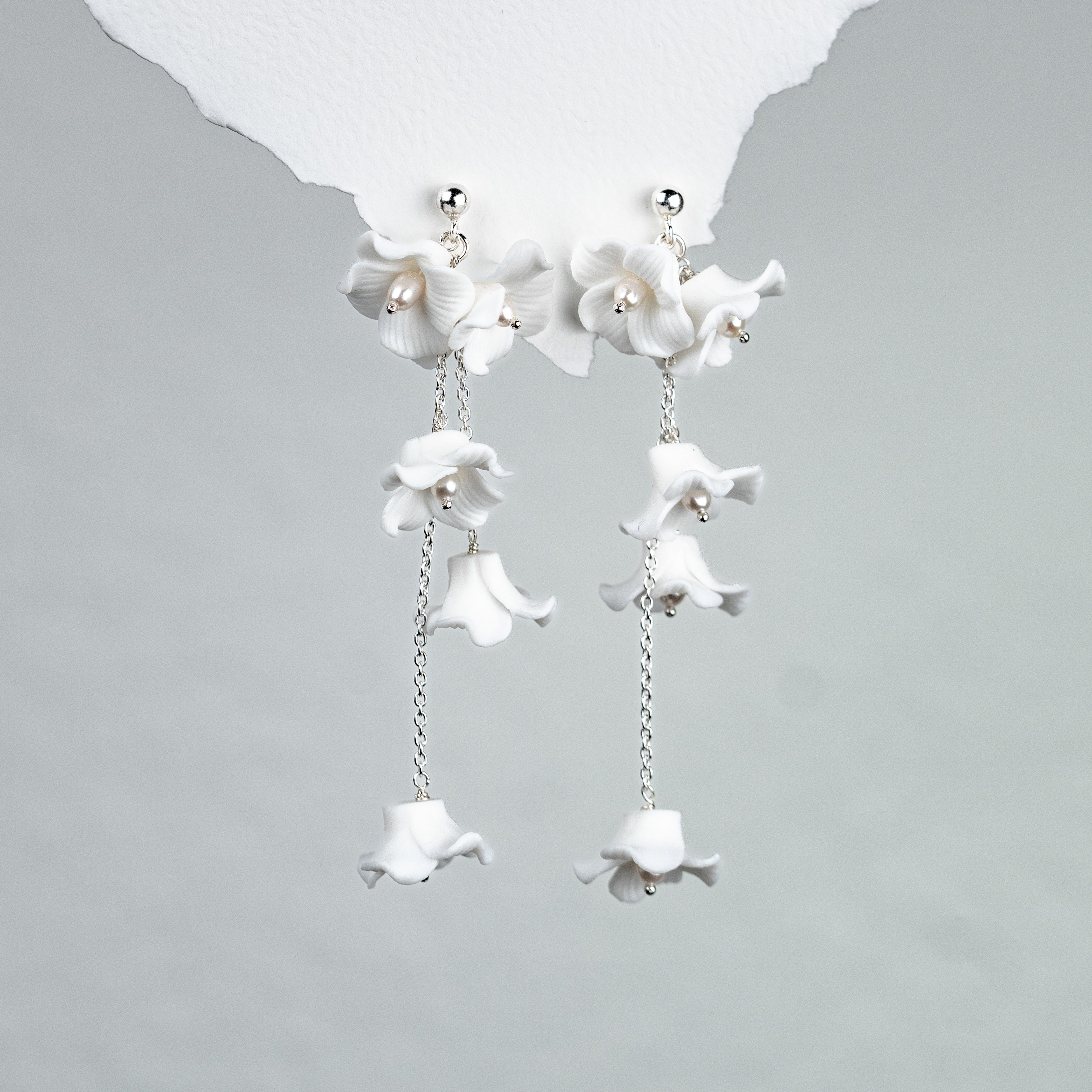 Elegante Brautohrringe aus 925er Sterlingsilber mit filigranen, beweglich hängenden Porzellanblüten, stilvoll präsentiert auf einer hellen Oberfläche.