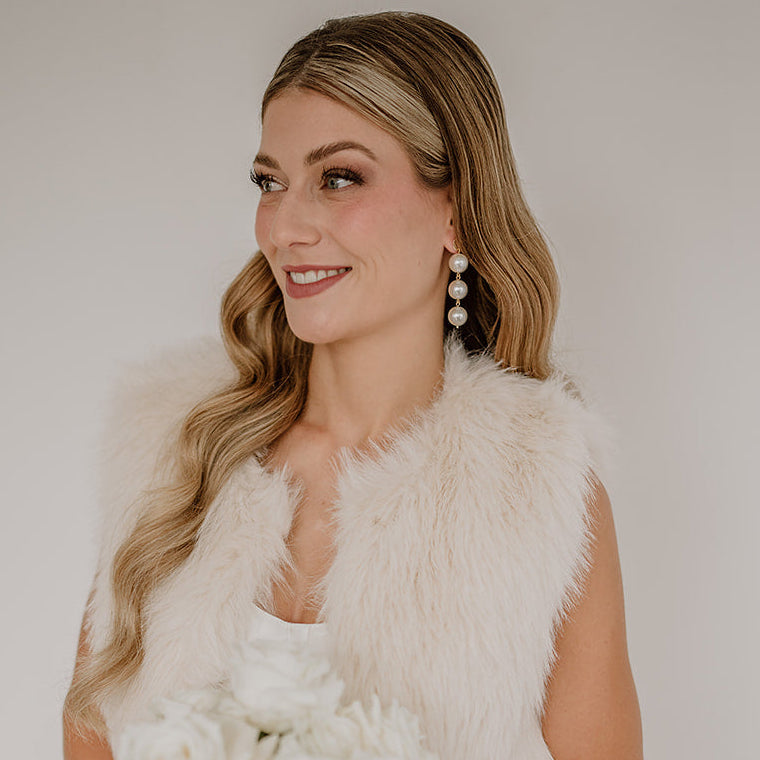 Elegante Brautohrringe aus 925er Sterlingsilber 18K vergoldet mit runden veganen Perlen untereinander hängend an einem schlichten, runden Plättchen Ohrstecker, stilvoll getragen von einem Model am Ohr und harmonisch kombiniert mit einer Brautfrisur und einem eleganten Brautlook.