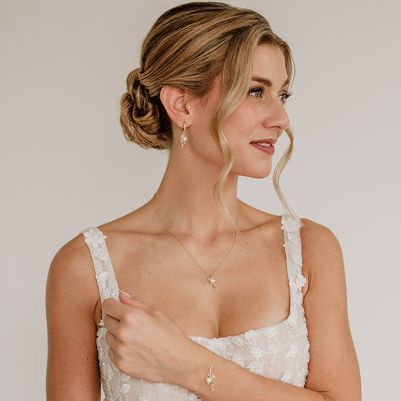 Model im weißen Brautkleid mit elegantem Hochsteckfrisur-Look, trägt 3-teiliges Schmuckset in 925er Silber 18K vergoldet bestehend aus Halskette, Creolen und Armband mit filigranen Blattanhängern, kleinen weißen Perlen und white opal Kristallperlen.